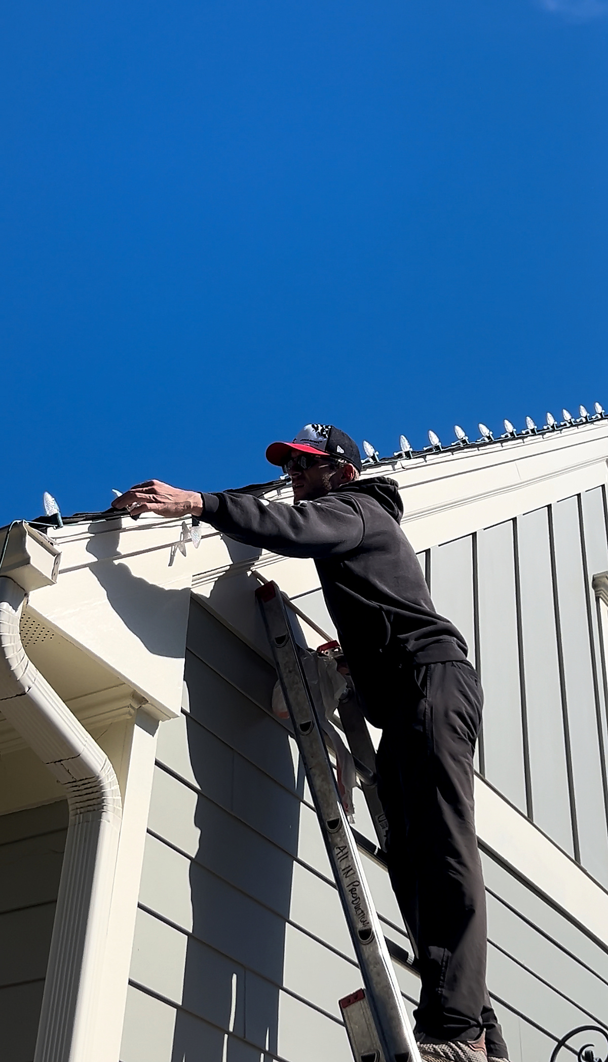 Christmas light installer hanging warm white lights on a ladder in Atlanta