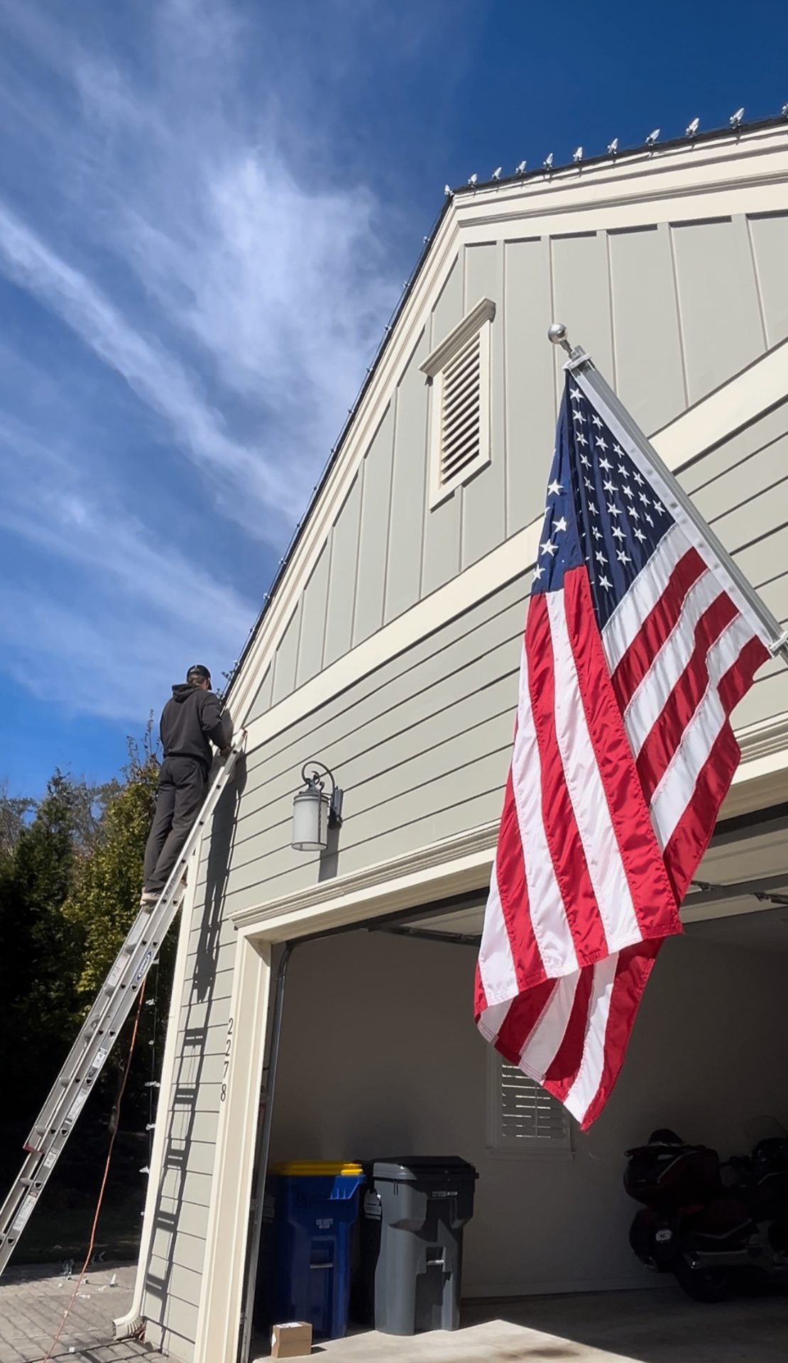Dreamland Christmas light installer on a ladder beside an American flag at an Atlanta home