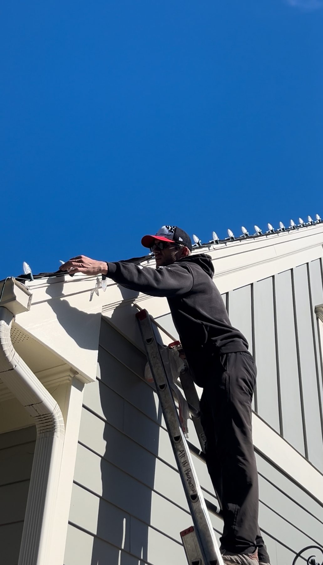Christmas light installer hanging warm white lights on a ladder in Atlanta