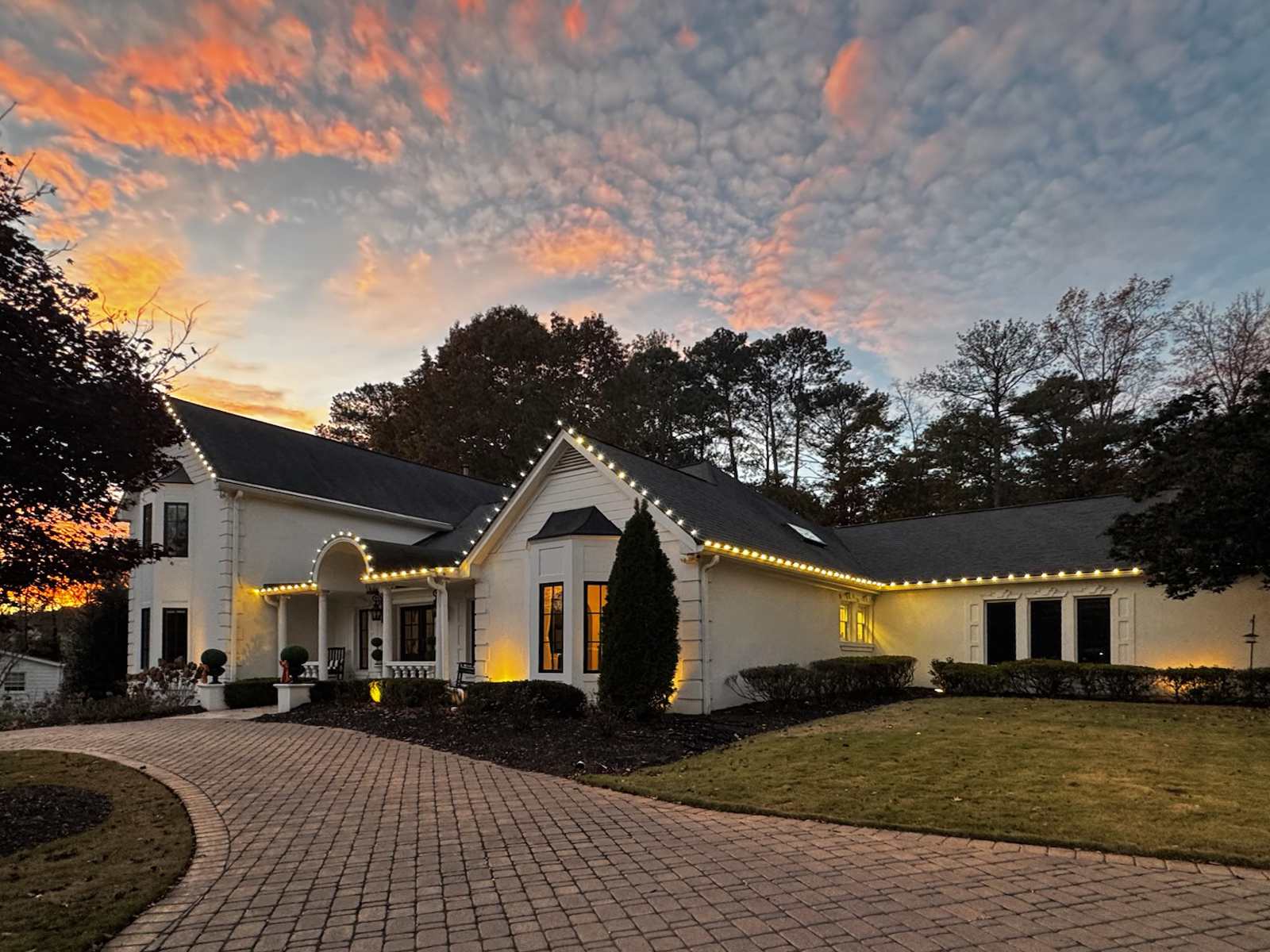 Professional Christmas light installer in Alpharetta GA on stucco estate at sunset
